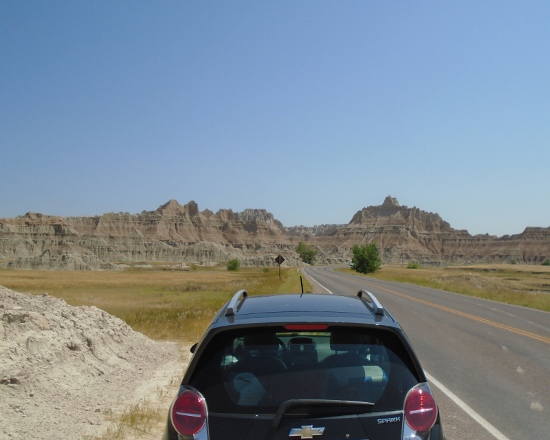 Photo of black car from the back looking toward the road, SD Badlands NP in the distance